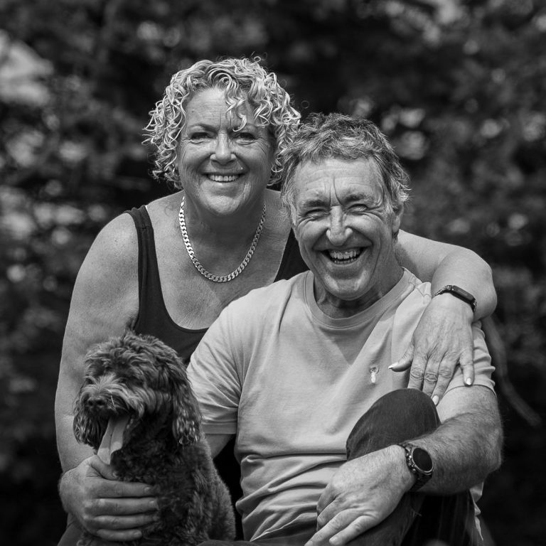 A smiling couple poses outdoors with a dog.